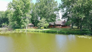 A lakeside cabin with a gazebo, surrounded by dense trees and a calm pond.