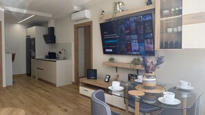Ett modernt kök med en inbyggd ugn, en matplats med ett glasbord och en platt-TV som är monterad på väggen och visar Disney-innehåll.