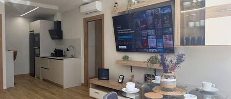 Una cocina moderna con horno integrado, una zona de comedor con mesa de vidrio y un televisor de pantalla plana montado en la pared que muestra contenido de Disney.