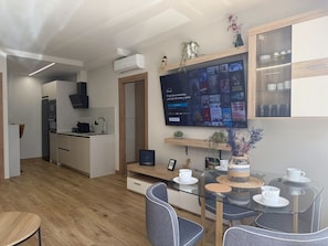 Een moderne keuken met een inbouwoven, een eethoek met een glazen tafel en een flatscreen-tv aan de muur waarop Disney te zien is.