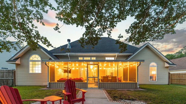 Una casa con un porche techado, mobiliario exterior y jardín.