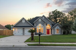 A two-story house with a garage, a red door, and a well-maintained lawn. - Savannah Family Hub: Game RM, Screened Porch & Work From Home, 15 mins Downtown (Pooler)
