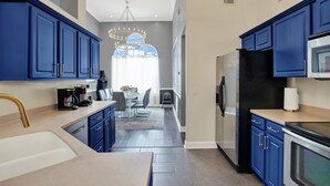 Una cocina moderna con armarios azules, electrodomésticos de acero inoxidable y un comedor con candelabro.
