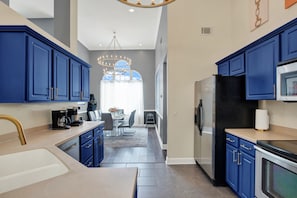 A modern kitchen with blue cabinets, stainless steel appliances, and a dining area with a chandelier. - Savannah Family Hub: Game RM, Screened Porch & Work From Home, 15 mins Downtown (Pooler)
