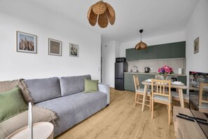 Ein modernes Apartment mit einem grauen Sofa, einem Esstisch mit Stühlen, einer Küchenzeile und einer hängenden gewebten Leuchte.