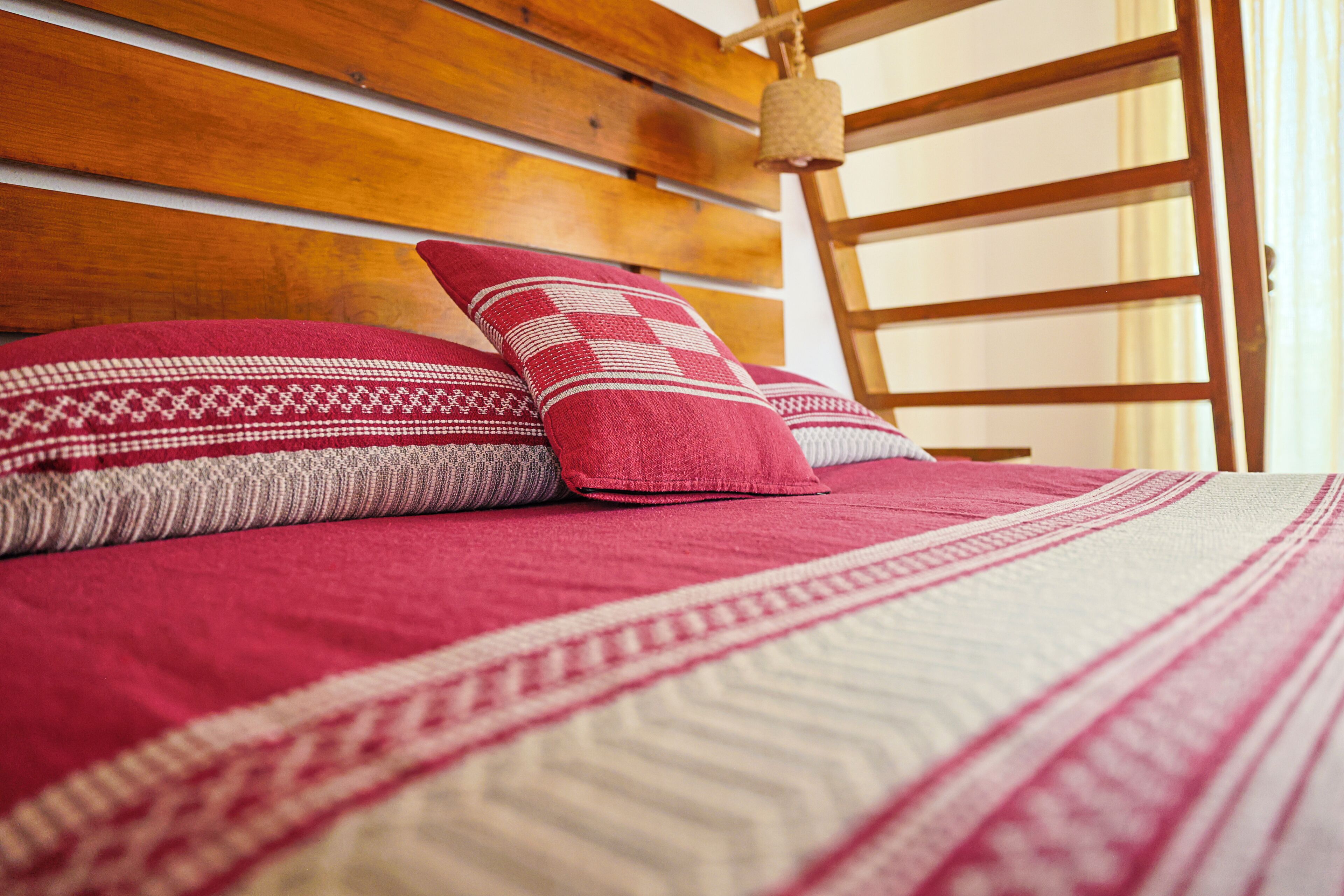 Ein Bett mit einem hölzernen Kopfteil, einer rot-weißen Decke und einem roten Kopfkissen.