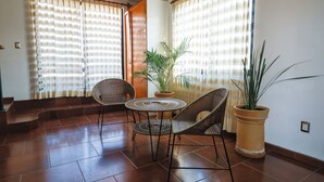 Una habitación con piso de baldosas, dos sillas de mimbre, una mesita redonda y una planta en maceta.