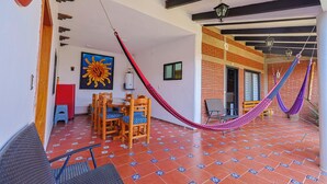 Una habitación con piso de baldosas, una mesa de comedor de madera con sillas, una hamaca y un cuadro grande de un sol.