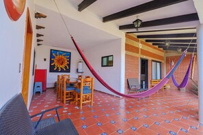 A room with a tiled floor, a wooden dining table with chairs, a hammock, and a large sun painting.
