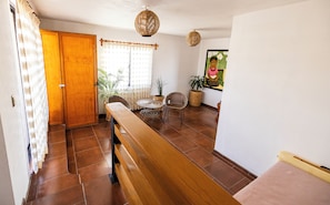 A hallway with a wooden bench, wicker chairs, a small round table, and potted plants.