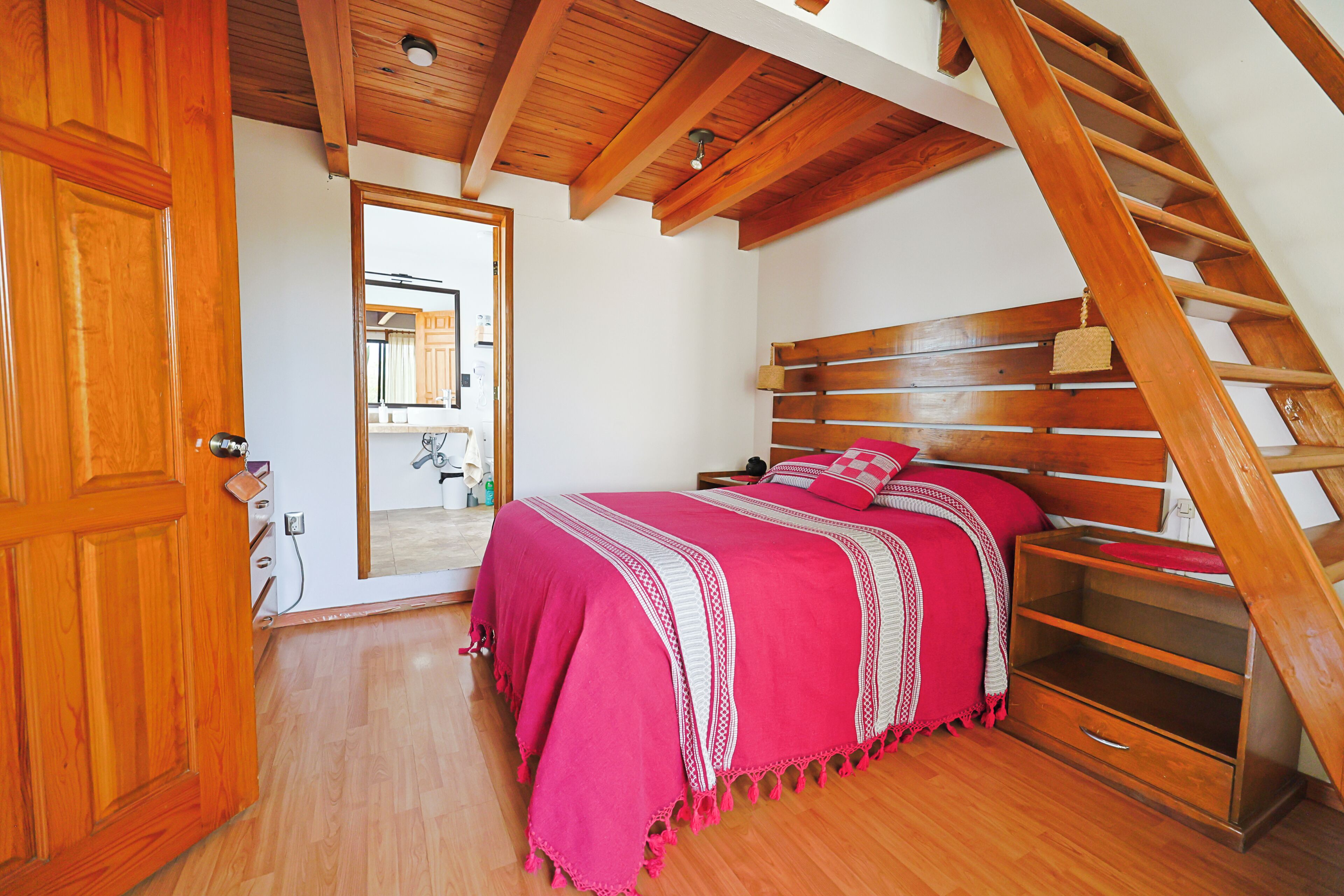 A bedroom with a wooden staircase, a bed with a pink blanket, and a wooden door.