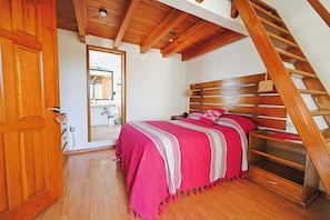 A bedroom with a wooden staircase, a bed with a pink blanket, and a wooden door.
