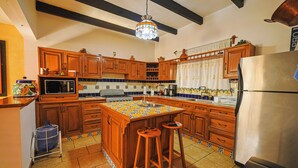 Una cocina con armarios de madera, una isla central con taburetes, un refrigerador de acero inoxidable y una lámpara colgante.