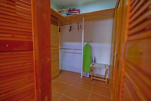 Una habitació amb un armari de fusta, una taula de planxar verda i una taula petita.