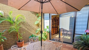 Un patio con una mesa, sillas, una sombrilla grande y plantas en macetas.