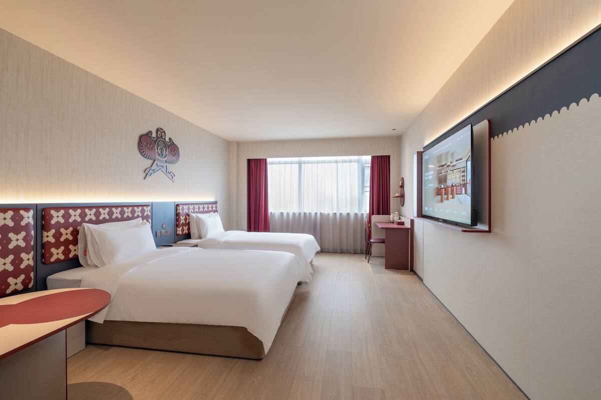 Ein Hotelzimmer mit zwei Betten, einem Schreibtisch, einem Sessel, einem Fernseher und einem Wanddekor.