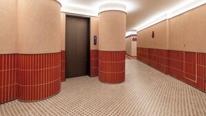 Un couloir d’hôtel aux murs rouges et beige, avec un sol à motifs et un ascenseur.
