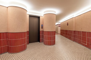 A hotel corridor with red and beige walls, a patterned floor, and an elevator. - Ni Hao Hotel Guangzhou Panyu Shiqiao (Guangzhou)