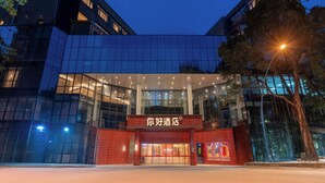 Un hôtel moderne avec une façade en verre, une entrée rouge et une enseigne dans une langue étrangère.