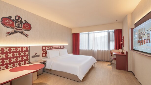 Une chambre d’hôtel avec un lit, un bureau, une chaise, une télévision et une fenêtre avec des rideaux.