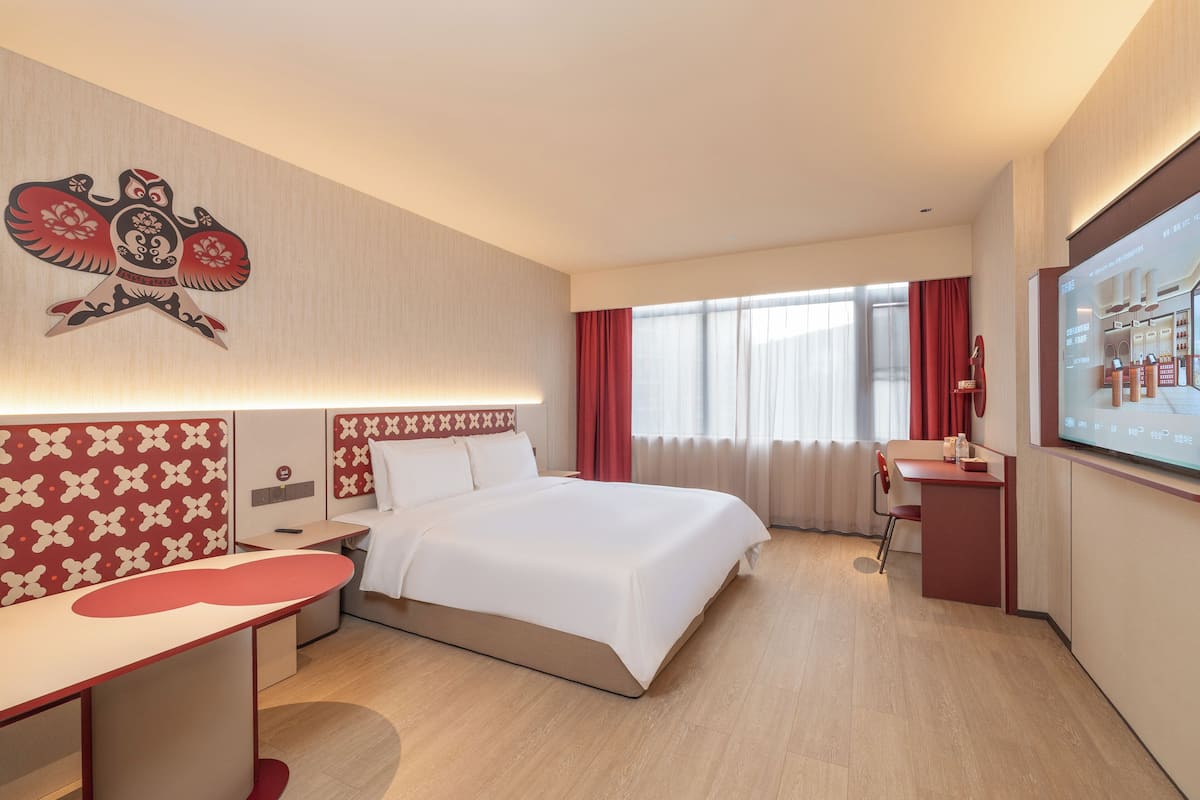Ein Hotelzimmer mit Bett, Schreibtisch, Stuhl, Fernseher und einem Fenster mit Vorhängen.