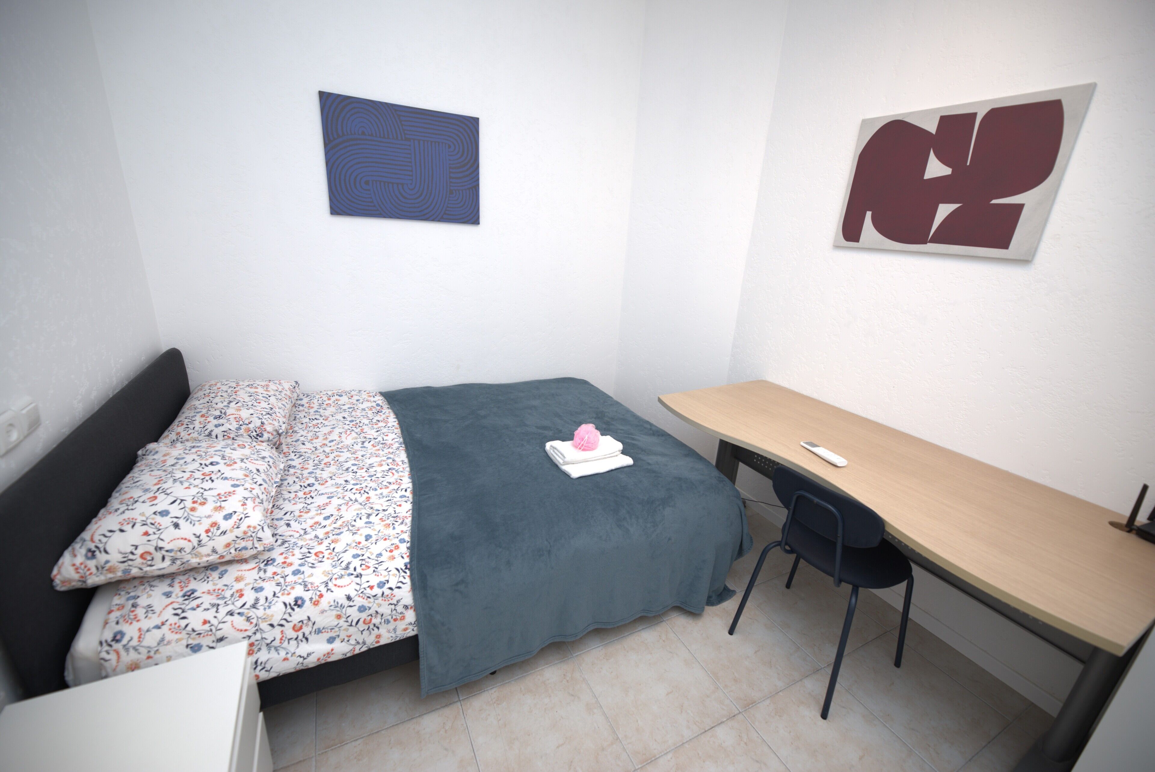 A small, neatly arranged bedroom with a bed, a desk, and a chair.