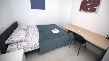 A small, neatly arranged bedroom with a bed, a desk, and a chair.