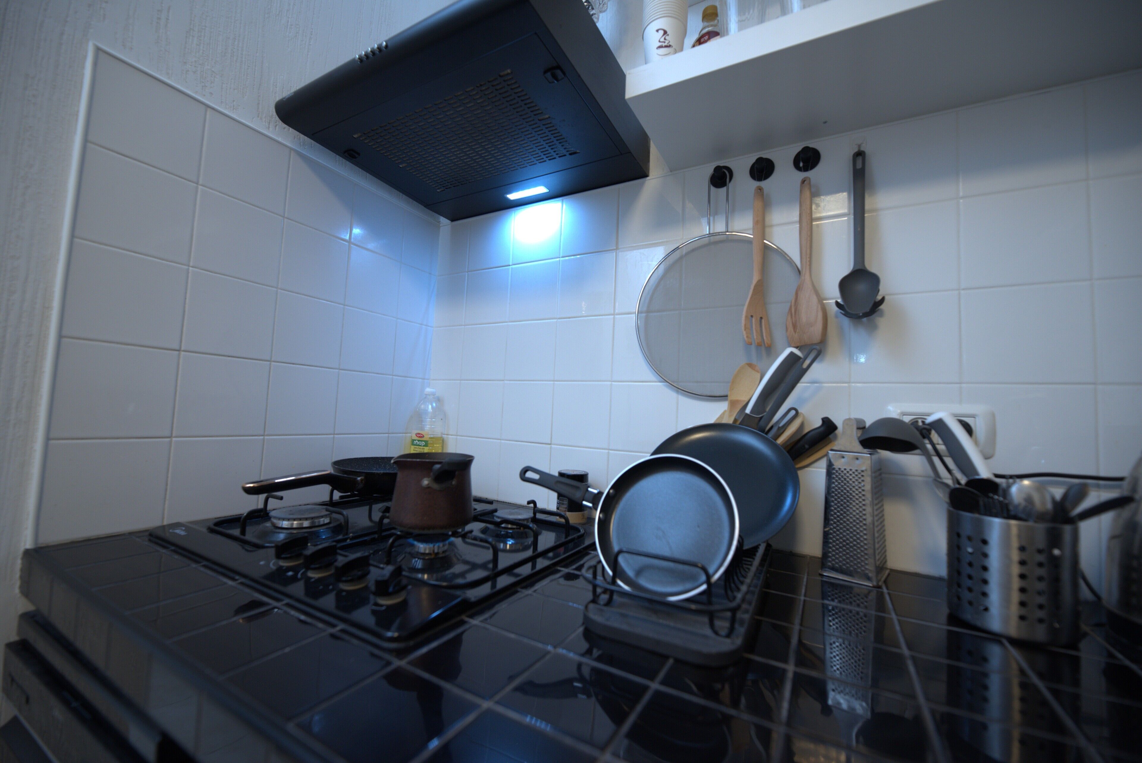 Una cocina con estufa a gas, ollas, sartenes y diferentes utensilios.