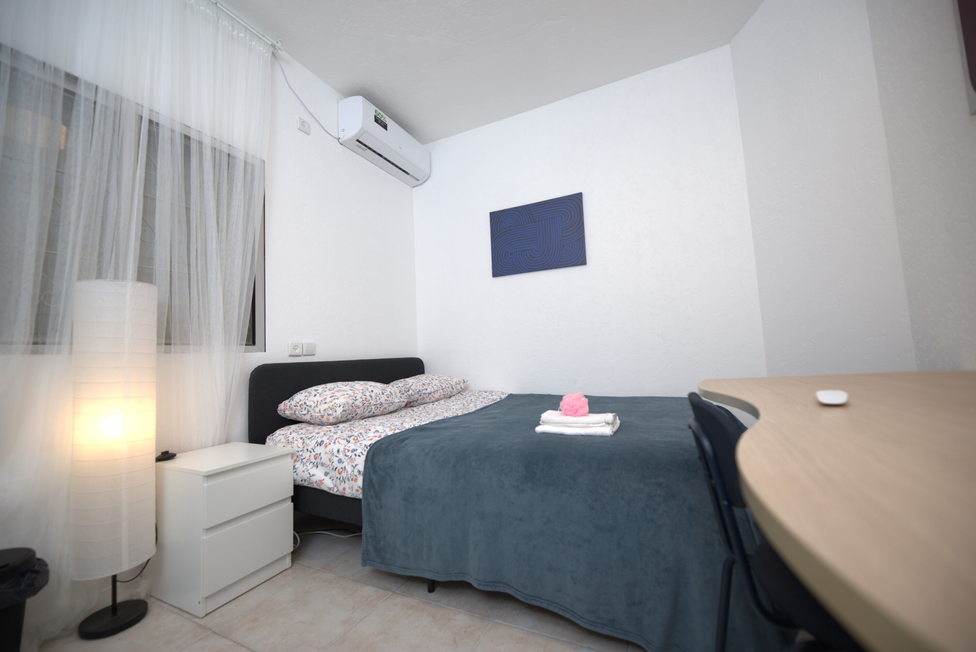 Un dormitorio pequeño y ordenado, con cama, mesita de noche y escritorio.