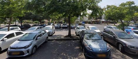 A parking lot with multiple cars parked under trees.