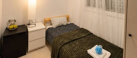 A small, clean room with a bed, a bedside table, a lamp, and an air conditioning unit.