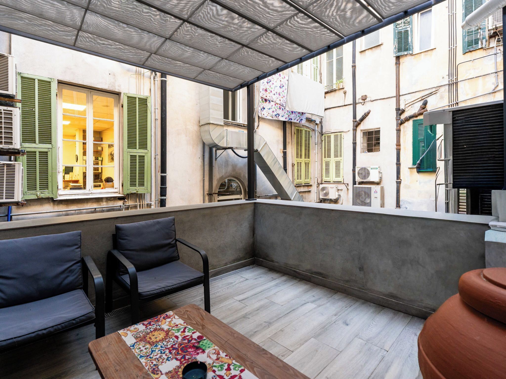 Une terrasse extérieure avec un espace salon, une table et une vue sur les bâtiments adjacents.