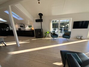 A spacious living area with a high ceiling, a fireplace, modern seating, and a large window providing a view of the outdoors.