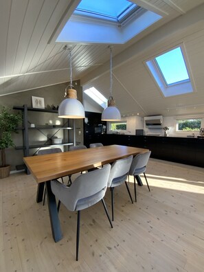 A modern kitchen with a skylight, wooden dining table, grey chairs, and a potted plant.