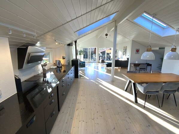 A modern kitchen with a large island, skylights, and a dining area with a wooden table and chairs.