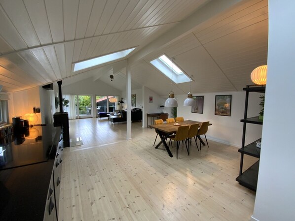 A spacious living area with a high ceiling, skylights, a dining table with chairs, and a kitchen area.