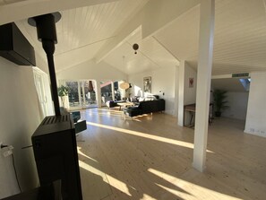 A spacious living area with a high ceiling, a fireplace, and a view through large glass doors to an outdoor patio.