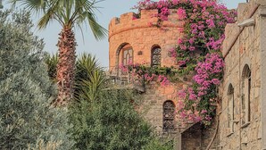 A stone building with arched windows and a balcony, surrounded by lush greenery and flowering plants. - Nurmahal Art & Heritage (Bodrum)