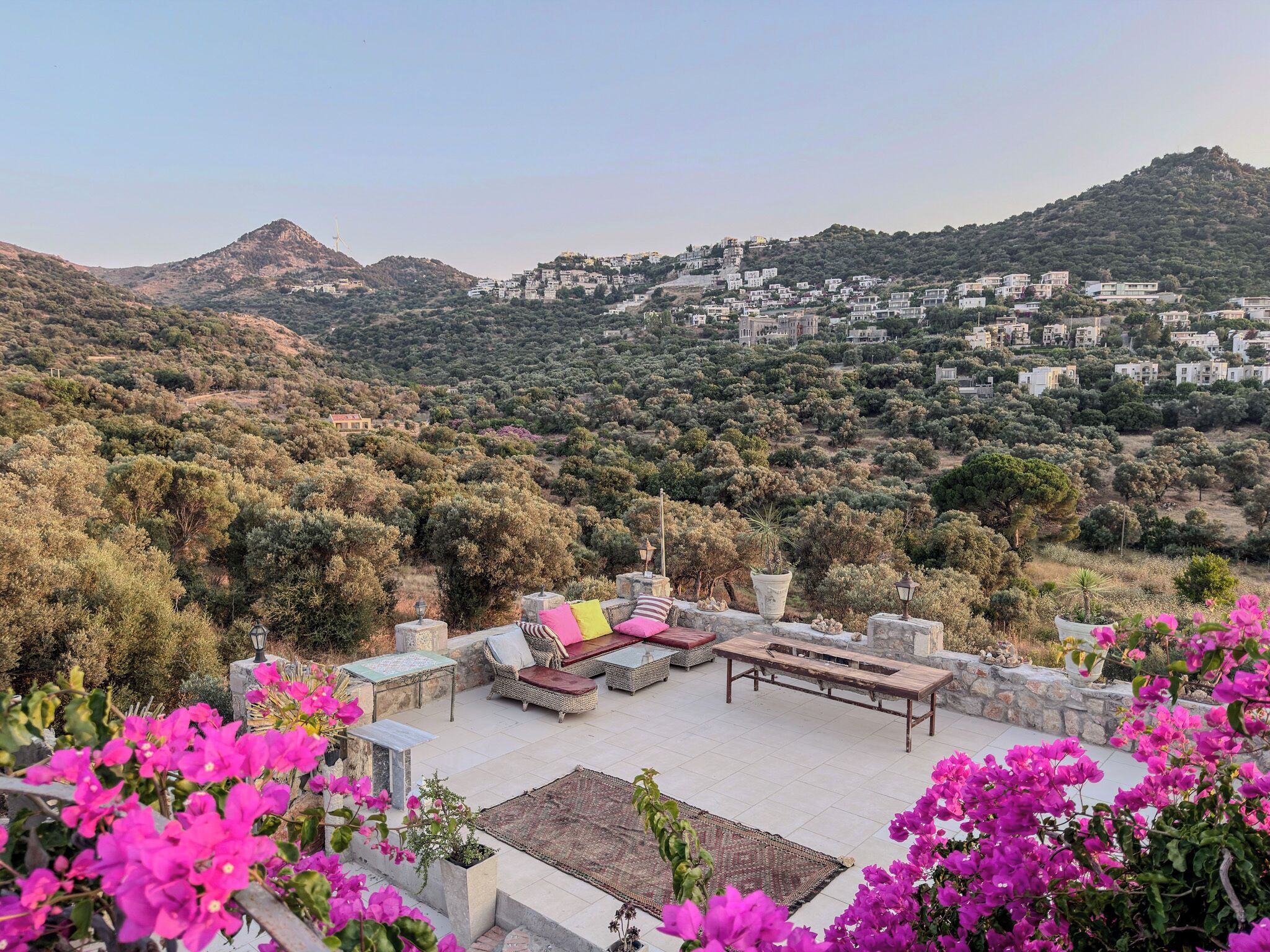 A terrace with outdoor furniture, a view of a hillside village, and bougainvillea flowers.