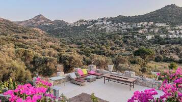A terrace with outdoor furniture, a view of a hillside village, and bougainvillea flowers.