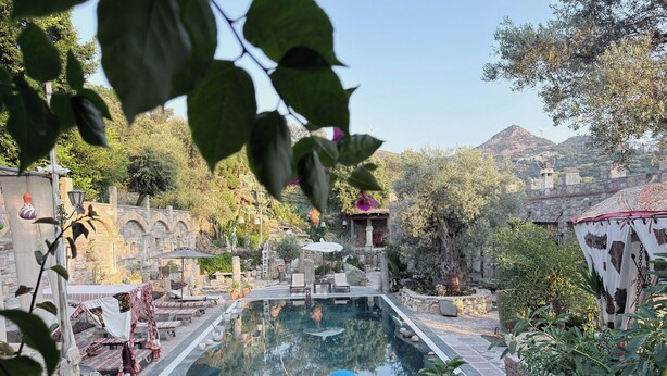 A pool area with stone architecture, a stone wall, and a view of hills. - Nurmahal Art & Heritage (Bodrum)