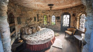 A stone-walled room with a round bed, a wooden chair, and a small table. - Nurmahal Art & Heritage (Bodrum)