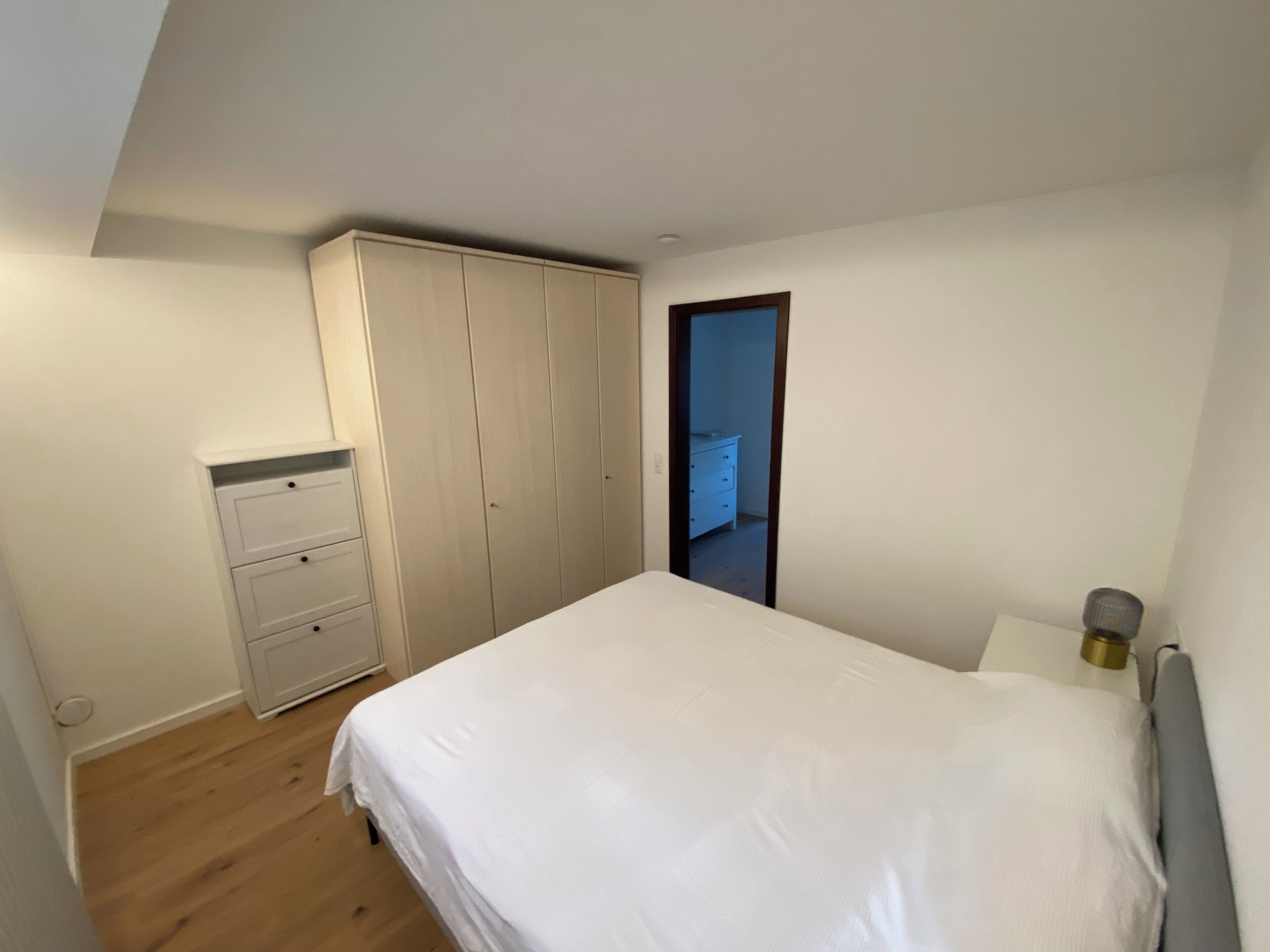Een slaapkamer met een bed, een kledingkast, een dressoir en een deur die naar een andere kamer leidt.