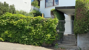 Ein modernes, zweistöckiges Haus mit geschlossenem Eingangstor, einem gepflegten Heckenstreifen und blauem Himmel.