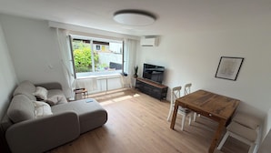 Ein modernes Wohnzimmer mit einer Couch, einem Holzespeiseplatz, einem Fernseher und einem Fenster mit Blick auf Grünflächen.
