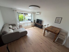 Ein modernes Wohnzimmer mit einer Couch, einem Holzespeiseplatz, einem Fernseher und einem Fenster mit Blick auf Grünflächen.