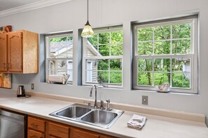 A kitchen with a double sink, wooden cabinets, and large windows with views of greenery. - Downtown 2 bedroom/2bath adorable, spacious bungalow (Hendersonville)