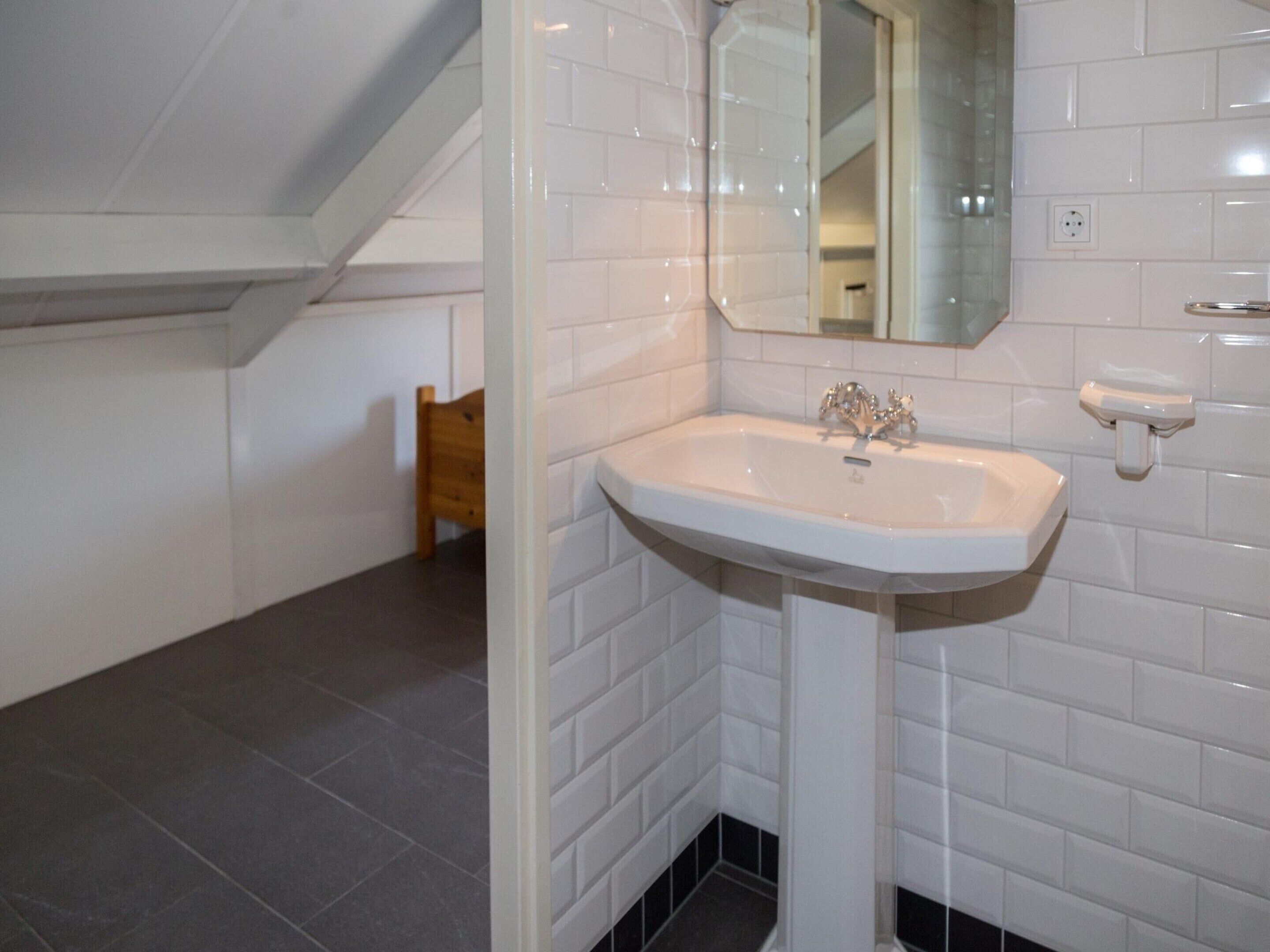 Une salle de bain avec des carreaux de céramique blancs rectangulaires, un lavabo blanc avec un seul robinet et un miroir au-dessus du lavabo.