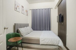 A small bedroom with a bed, a green chair, a television, and a door. - Cozy Stay at Winland Tower Residences (Quezon City)