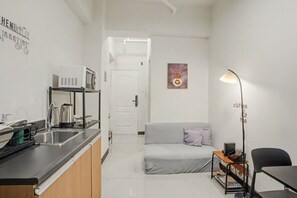 A compact living space with a kitchenette, a sofa, a coffee table, and a floor lamp. - Cozy Stay at Winland Tower Residences (Quezon City)